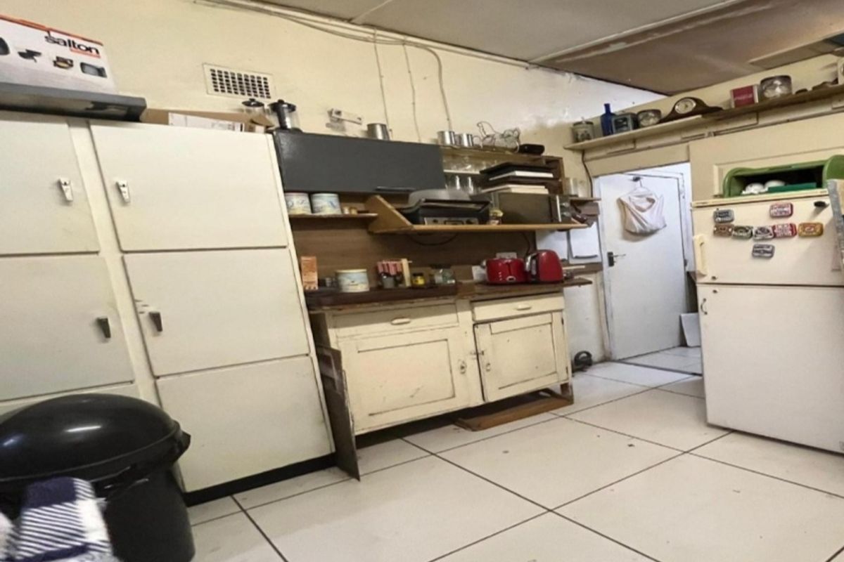 A dated kitchen area featuring original cabinetry, tiled flooring, and exposed ceiling details, requiring significant renovation to modernize the space.