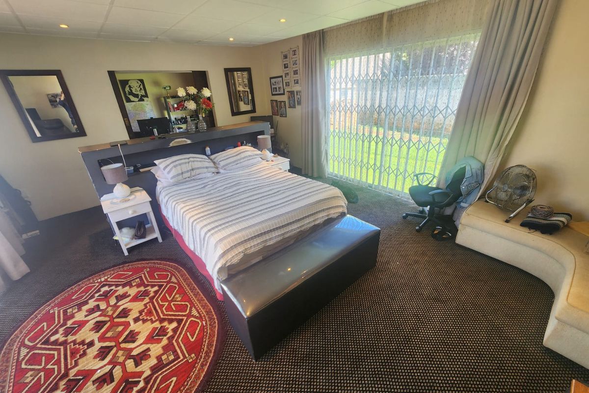 Spacious bedroom featuring a built-in headboard partition, recessed ceiling lighting, and large sliding glass doors with security gates leading to the garden.