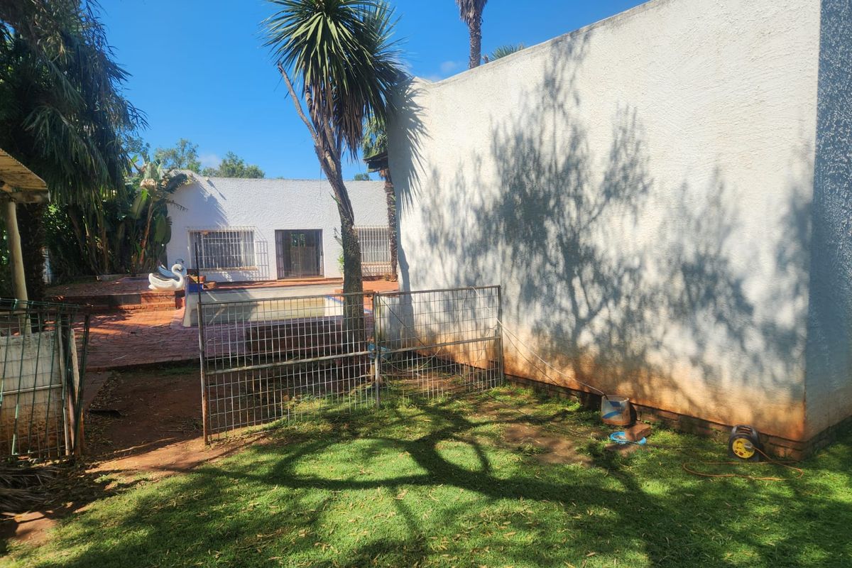 Rear garden area featuring a swimming pool, paved patio, and a large exterior wall with visible weathering and staining.