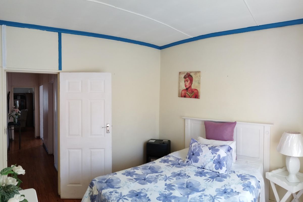 A bedroom featuring wooden flooring and a white panel door, leading into an adjacent hallway.