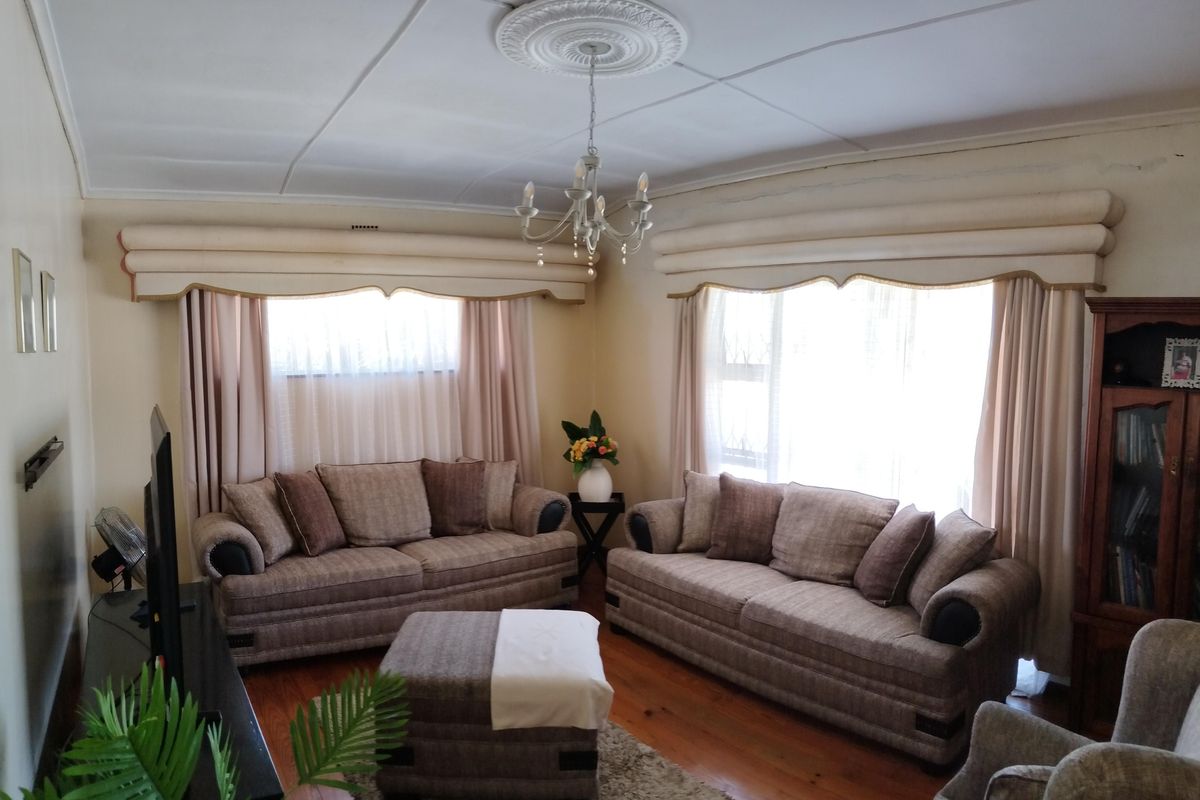A traditional living room featuring hardwood flooring, decorative ceiling rose, and large windows with built-in pelmets.