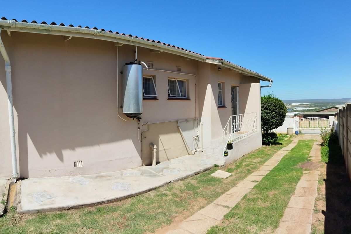 Rear exterior view of the house featuring a paved walkway, external geyser unit, and access to the backyard area.