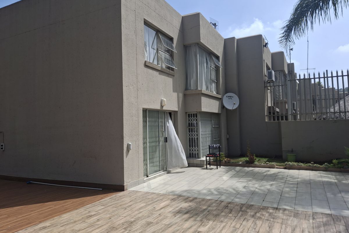 Rear view of the townhouse featuring a paved patio area, sliding glass doors, security gates, and exterior wall finishes.