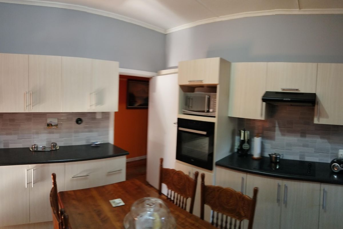 A functional kitchen featuring light-toned cabinetry, dark countertops, a built-in oven, and a modern extractor fan with tiled splashbacks.