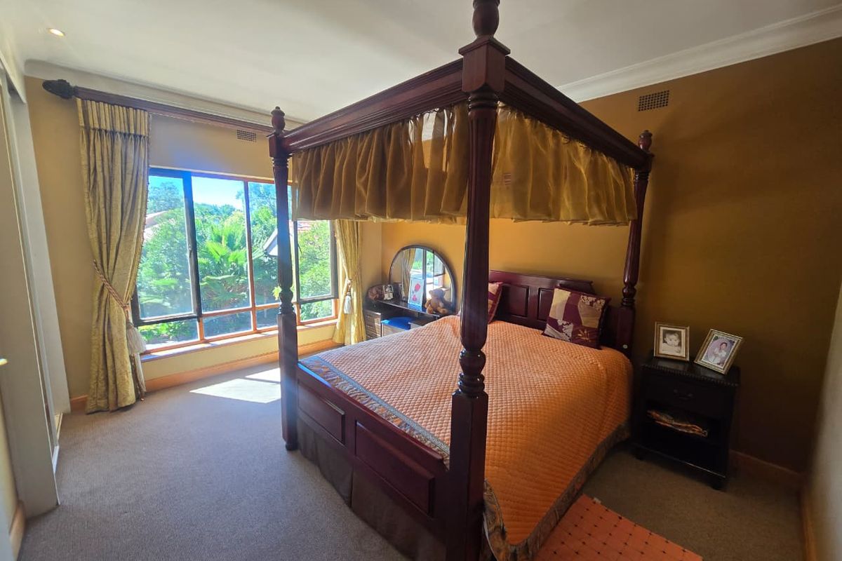 A spacious bedroom featuring neutral carpeting, coving, and a large window providing natural light and garden views.