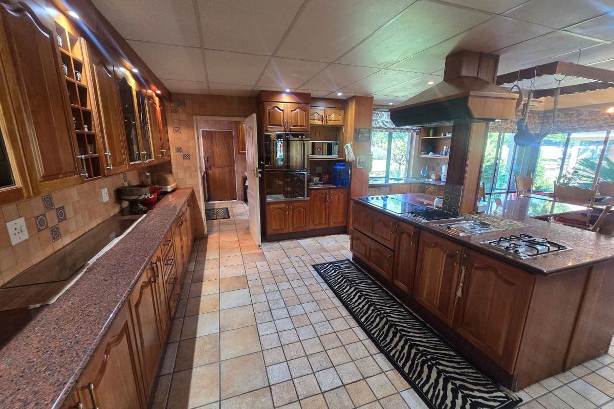 Spacious kitchen featuring extensive wooden cabinetry, granite countertops, a central island with a gas hob, and integrated appliances.