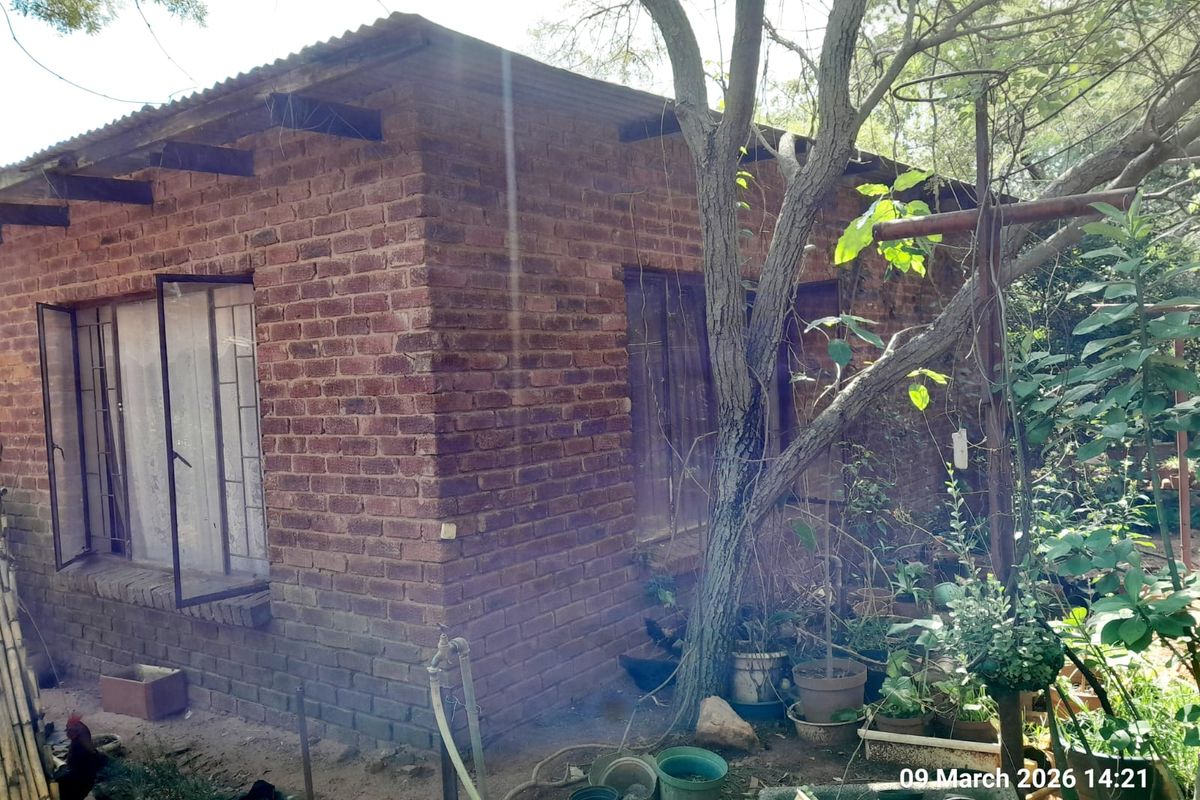 A rustic brick outbuilding featuring exposed rafters and metal-framed windows, situated in a garden setting on the farm property.