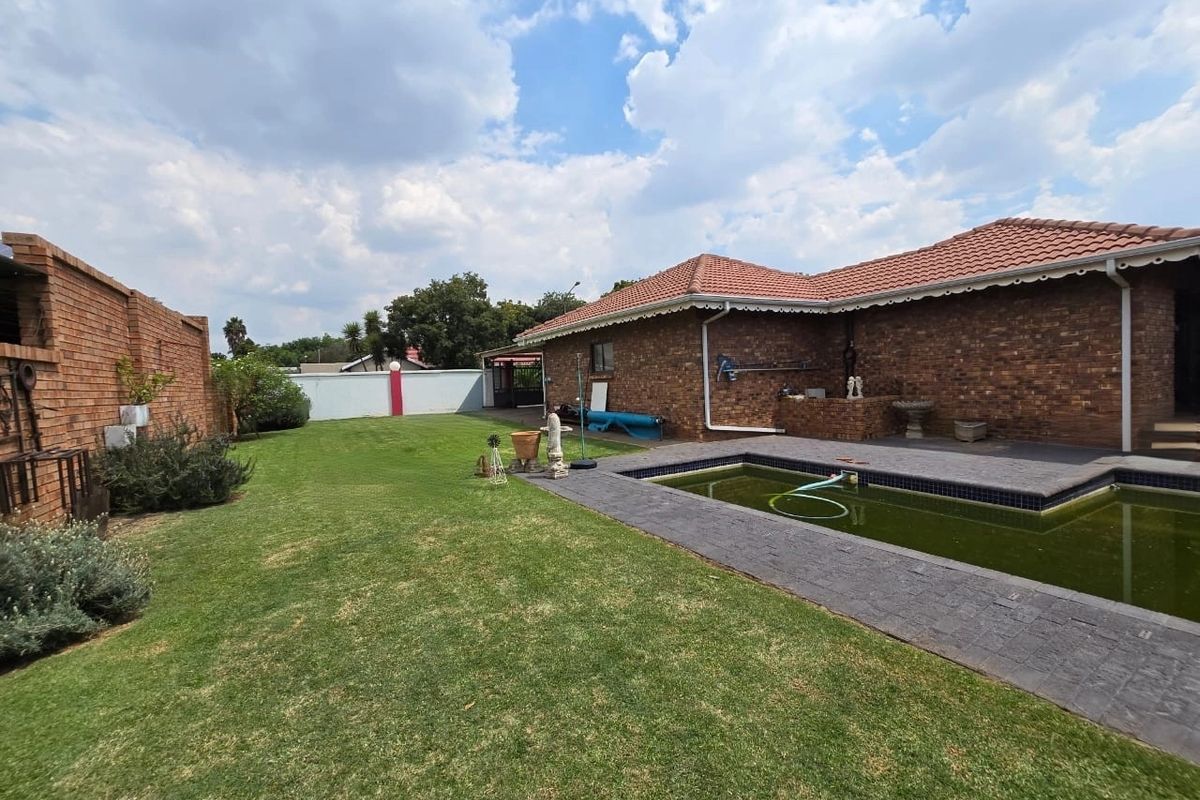 Rear garden area featuring a brick-clad house exterior, a swimming pool with paved surround, and a spacious lawn.