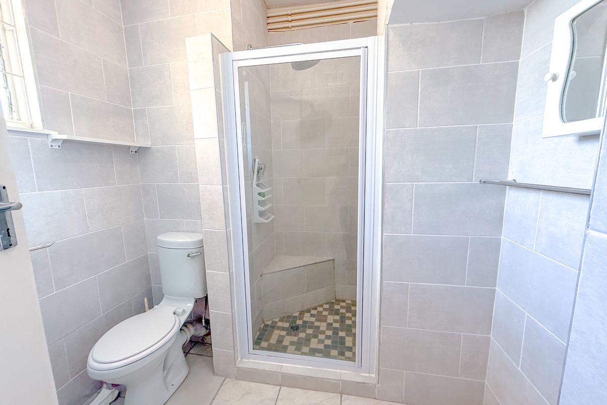 A functional bathroom featuring a glass-enclosed shower with a built-in seat, a standard toilet, and neutral wall tiling throughout.