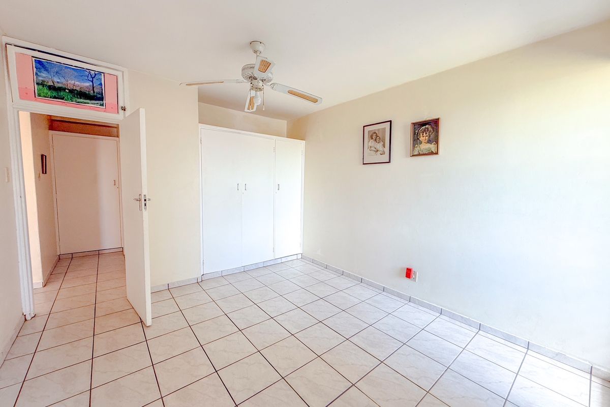 A bright, empty bedroom featuring neutral tiled flooring, built-in wardrobe storage, and a ceiling fan, offering a clean canvas for personalization.