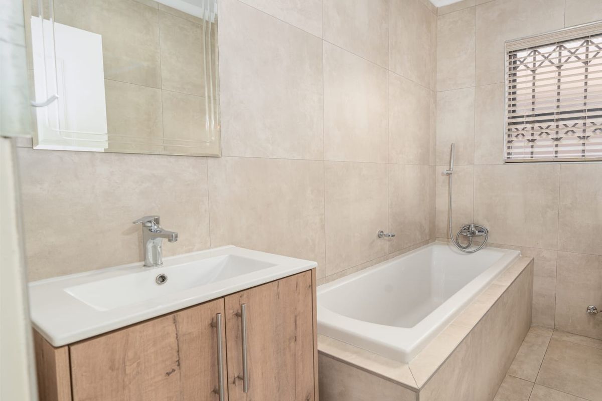 Modern bathroom featuring neutral floor-to-ceiling tiling, a built-in bathtub with shower mixer, and a contemporary vanity unit with a wall-mounted mirror.