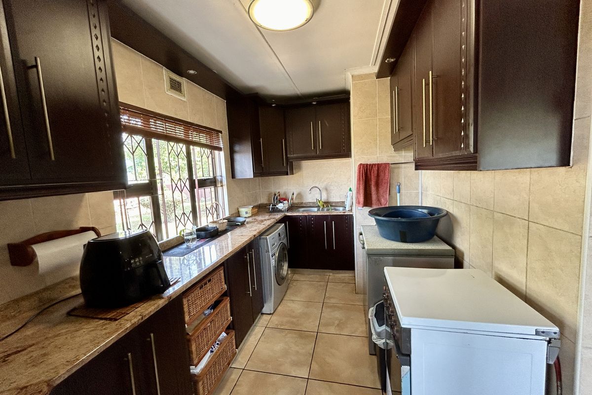 A functional kitchen featuring dark wood cabinetry, granite countertops, tiled flooring, and integrated space for laundry appliances.