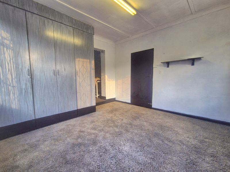 A vacant bedroom featuring built-in cupboards, carpet flooring, and a wall-mounted shelf, offering a blank canvas for renovation or restyling.