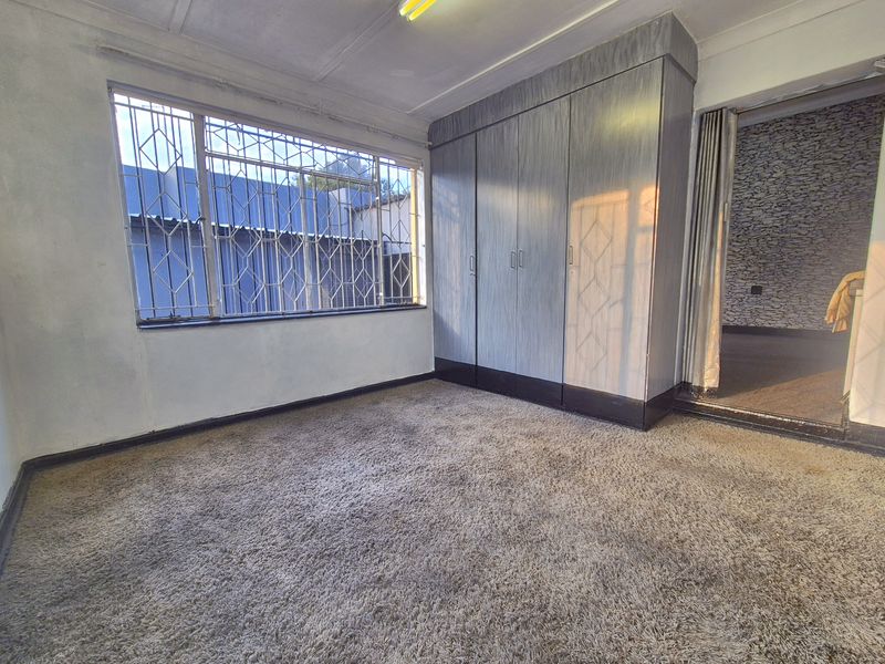 An empty bedroom featuring built-in cupboards, security bars on the windows, and carpeted flooring, offering a blank canvas for renovation.