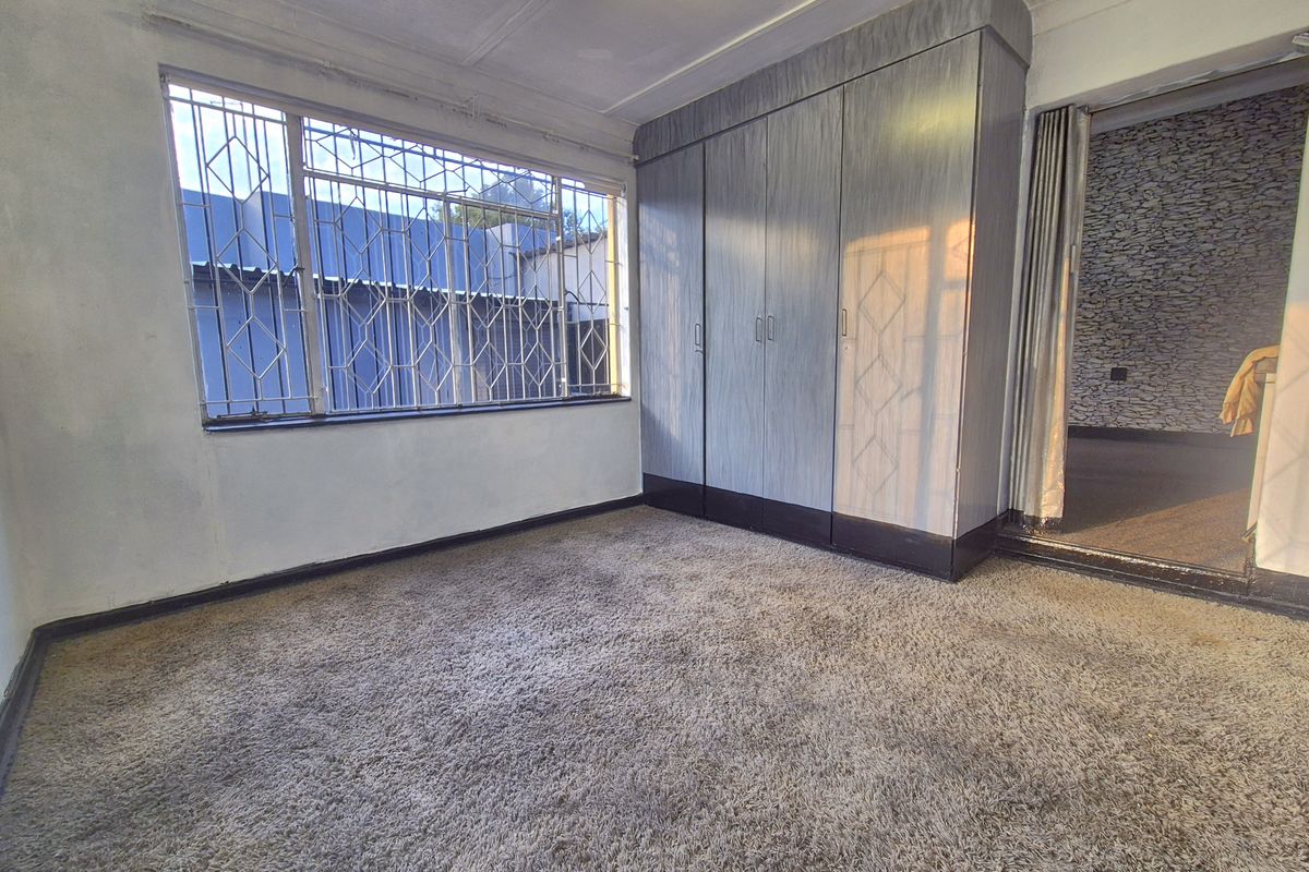 An empty bedroom featuring built-in cupboards, security bars on the windows, and carpeted flooring, offering a blank canvas for renovation.