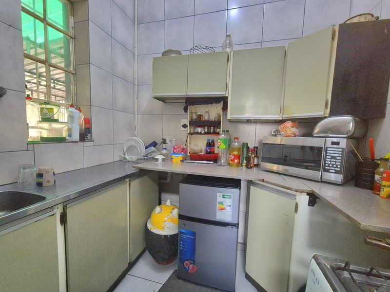 A compact, dated kitchen featuring tiled walls, laminate countertops, and built-in cabinetry, offering potential for a modern renovation.