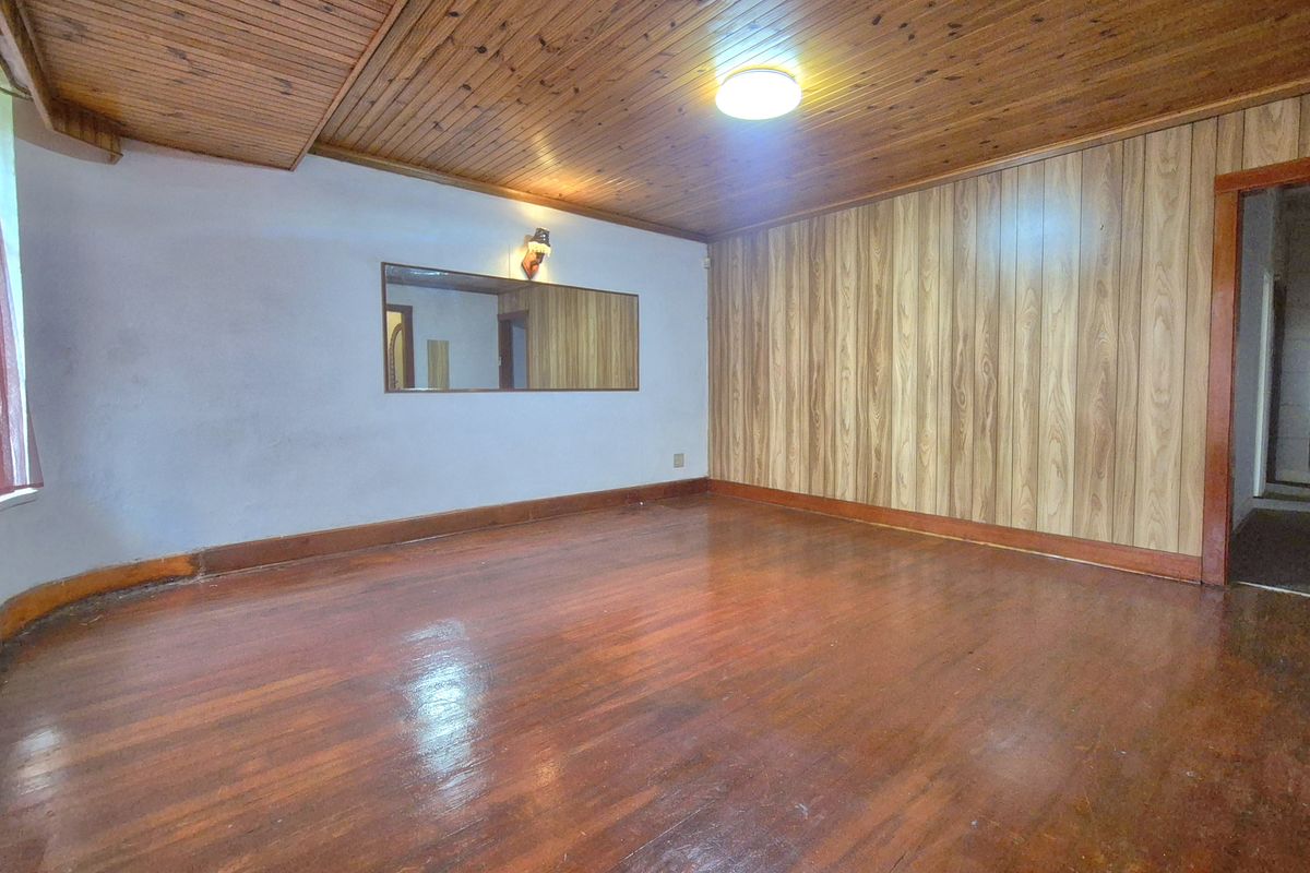An empty living room featuring timber ceiling paneling, wood-paneled feature wall, and polished hardwood flooring with a wall-mounted mirror.