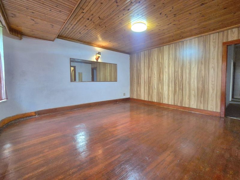 An empty living room featuring timber ceiling paneling, wood-paneled feature wall, and polished hardwood flooring with a wall-mounted mirror.
