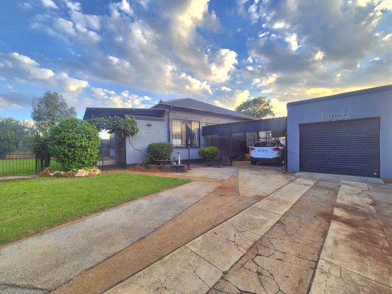 Front exterior view of the house featuring a paved driveway, attached garage with roller shutter door, carport, and security features.