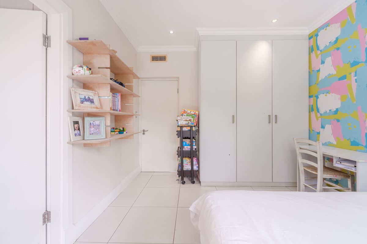 A bright bedroom featuring built-in floor-to-ceiling wardrobes, tiled flooring, recessed downlighting, and custom wall-mounted shelving.