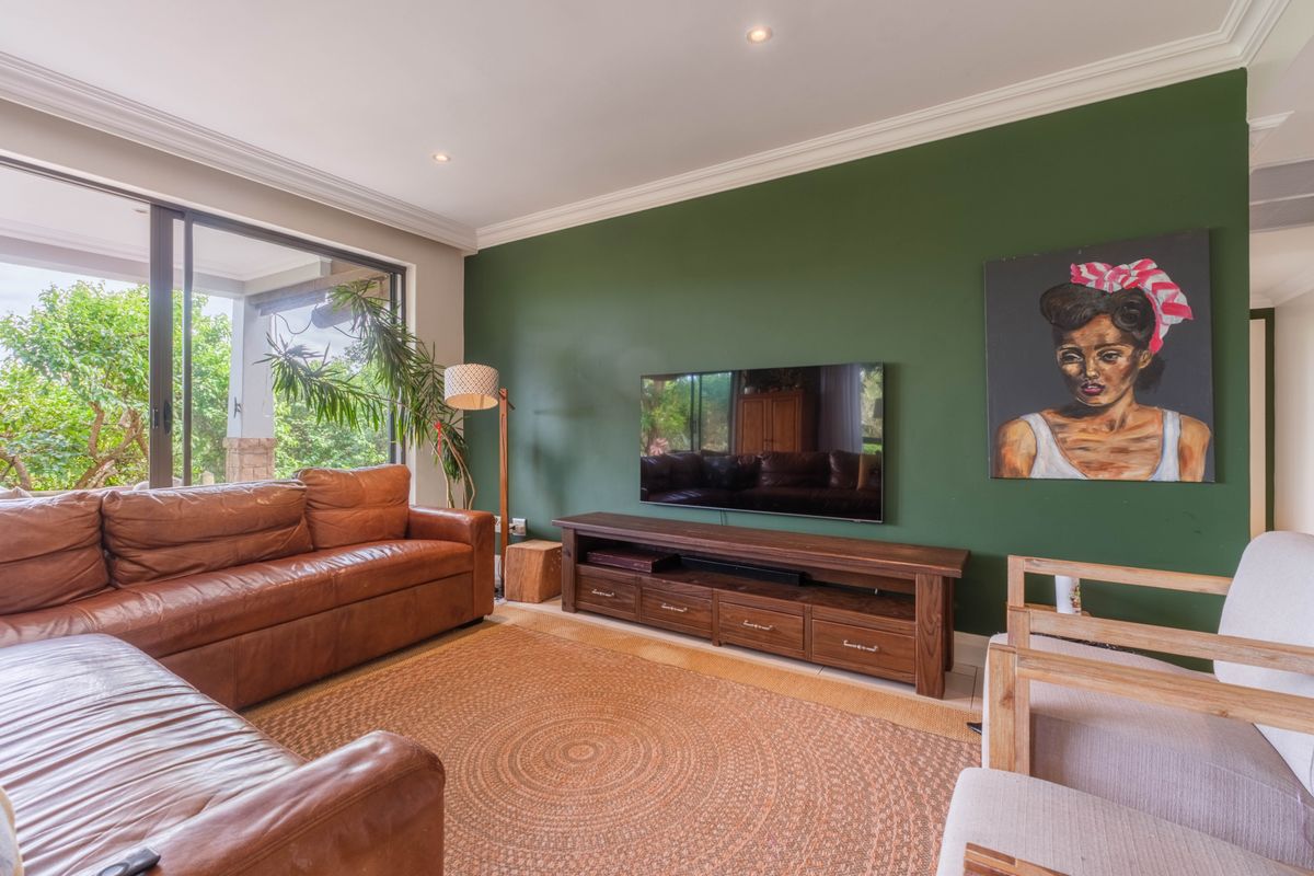A comfortable living room featuring a bold green accent wall, recessed ceiling lighting, and large sliding glass doors leading to an outdoor patio area.
