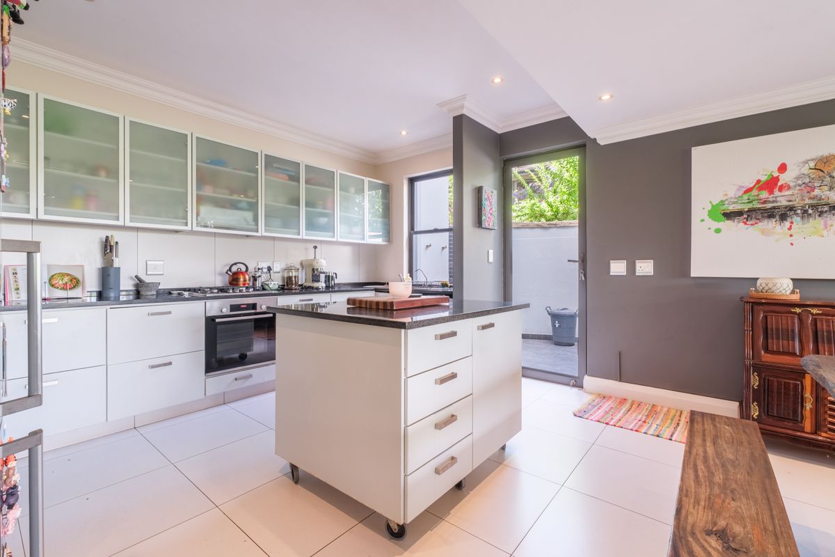 Modern kitchen featuring white cabinetry, a central mobile island with stone countertop, integrated oven, and direct access to a private rear courtyard.