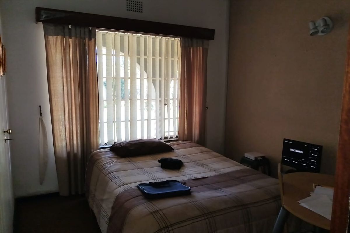 A bedroom featuring a window with vertical blinds and a wooden pelmet, providing natural light and a view of the exterior.