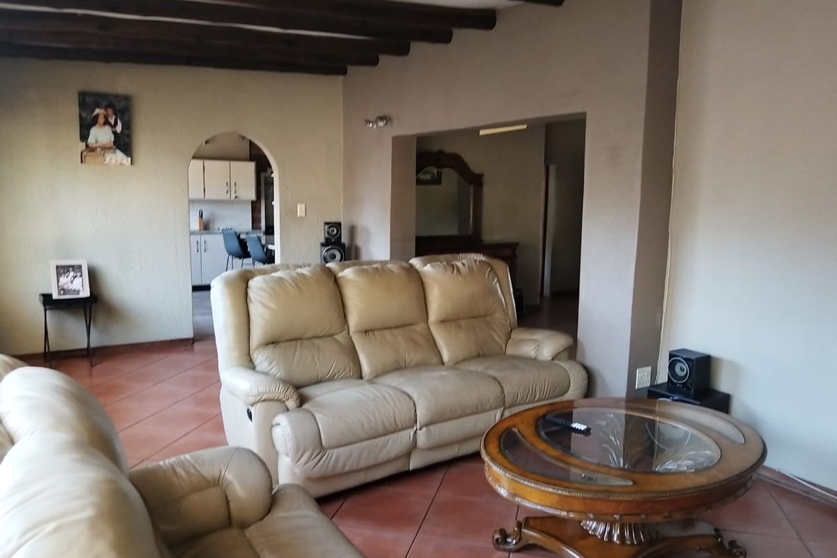 A living room featuring exposed timber ceiling beams and terracotta floor tiles, with an arched doorway leading to the kitchen area.