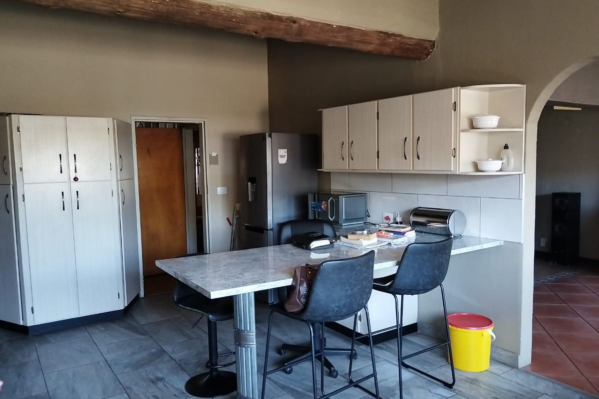 A functional kitchen area featuring light-toned cabinetry, a stone-look breakfast bar, and tiled flooring, complemented by an exposed timber ceiling beam.