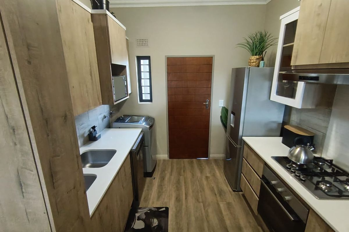 Modern galley-style kitchen featuring wood-grain cabinetry, stone countertops, integrated gas hob, built-in oven, and stainless steel sink.