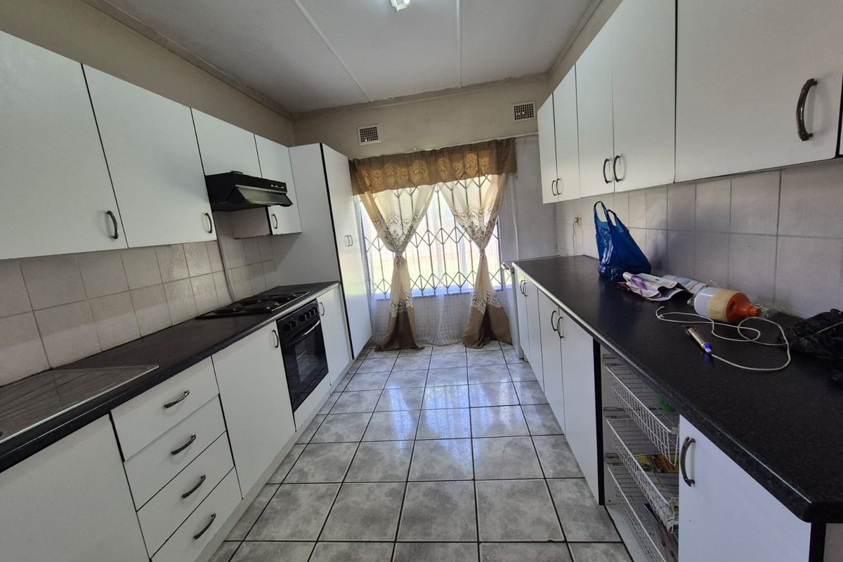 Functional galley-style kitchen featuring white cabinetry, dark countertops, built-in oven, hob, and extractor fan with tiled flooring.