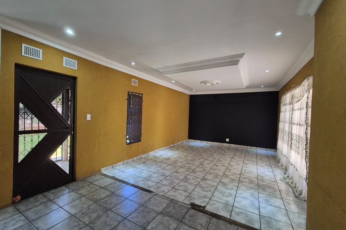 An empty living room featuring mustard and black accent walls, recessed ceiling lighting, and tiled flooring with visible damage.