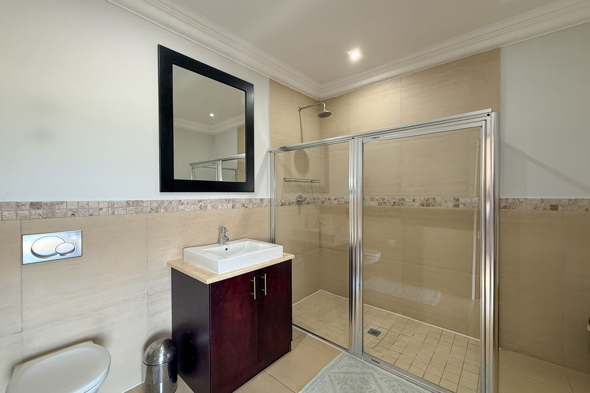 A modern bathroom featuring a glass-enclosed shower, a vanity with a vessel sink, and a wall-mounted toilet with a dual-flush plate.