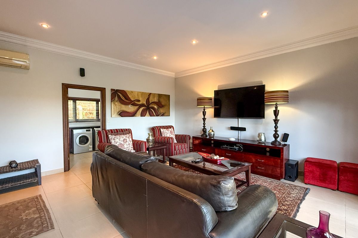 A comfortable living room featuring tiled flooring, recessed ceiling lighting, and a wall-mounted air conditioning unit, with an adjacent laundry area visible.