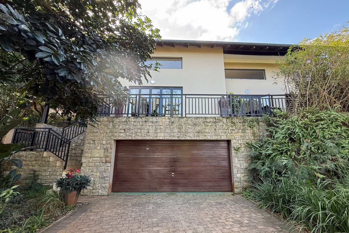 Rear exterior view of the property featuring a stone-clad base, integrated garage, and an elevated balcony with metal railings.