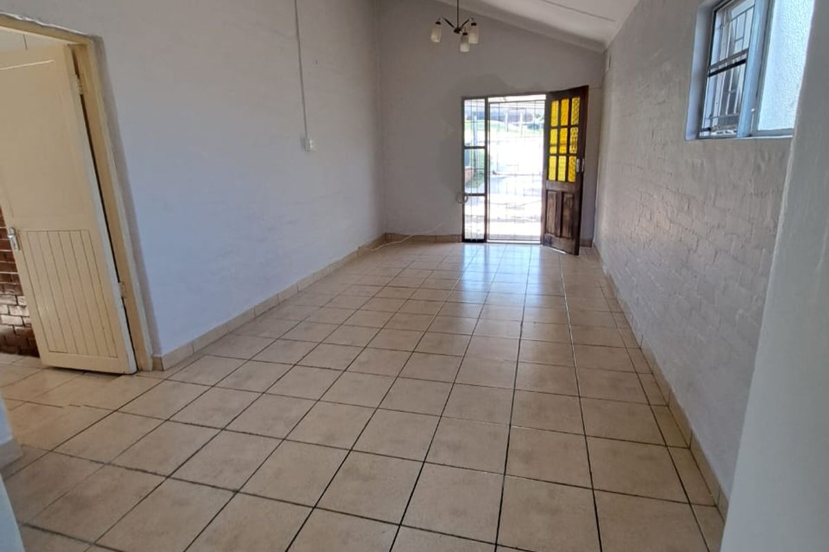 An empty, open-plan living area featuring tiled flooring, a raked ceiling, and direct access to the exterior through a security gate.