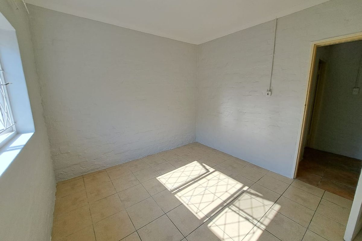 An empty bedroom featuring tiled flooring, painted brick walls, and a window with security bars.
