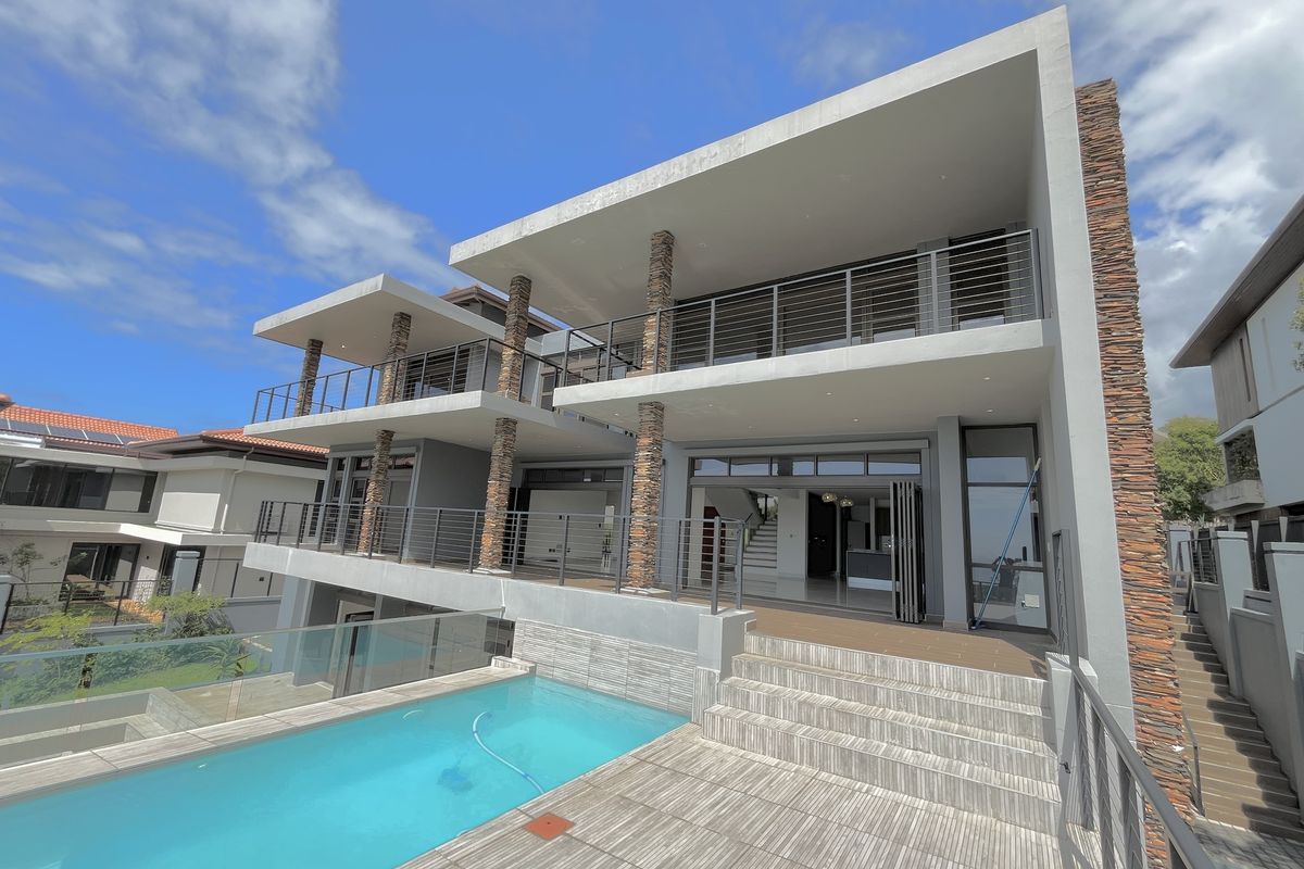 Modern multi-level rear exterior featuring a swimming pool, expansive tiled patio, stone-clad columns, and large sliding glass doors leading to the interior.