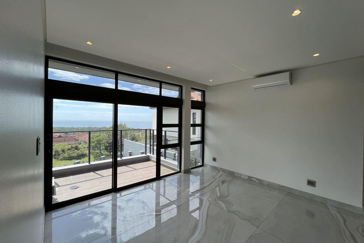 Modern, empty bedroom featuring large format polished tiles, recessed lighting, air conditioning, and expansive sliding doors opening onto a balcony with scenic views.