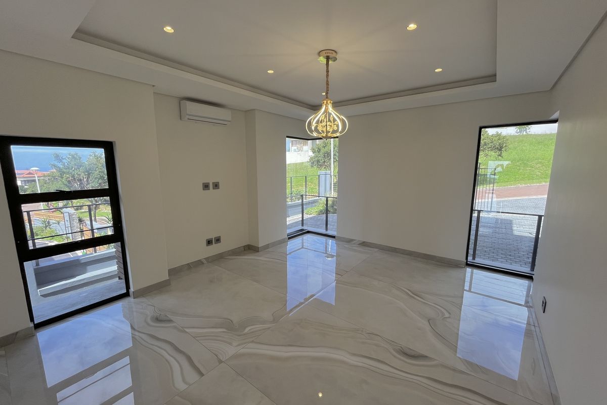 A bright, modern, and empty living room featuring large-format polished porcelain tiles, recessed ceiling lighting, and multiple windows providing natural light.
