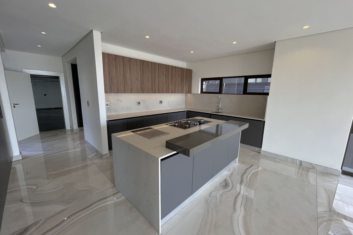 Modern kitchen featuring a central island with built-in hob, stone countertops, sleek cabinetry, and polished large-format porcelain floor tiles.