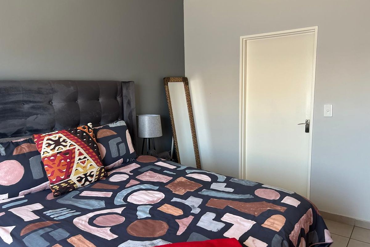 A well-maintained bedroom featuring neutral wall tones, a feature wall, and tiled flooring.