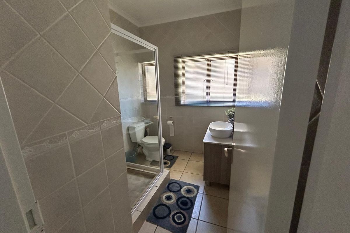 A functional bathroom featuring a glass-enclosed shower, a modern vessel sink vanity, and tiled flooring with neutral wall tiles.