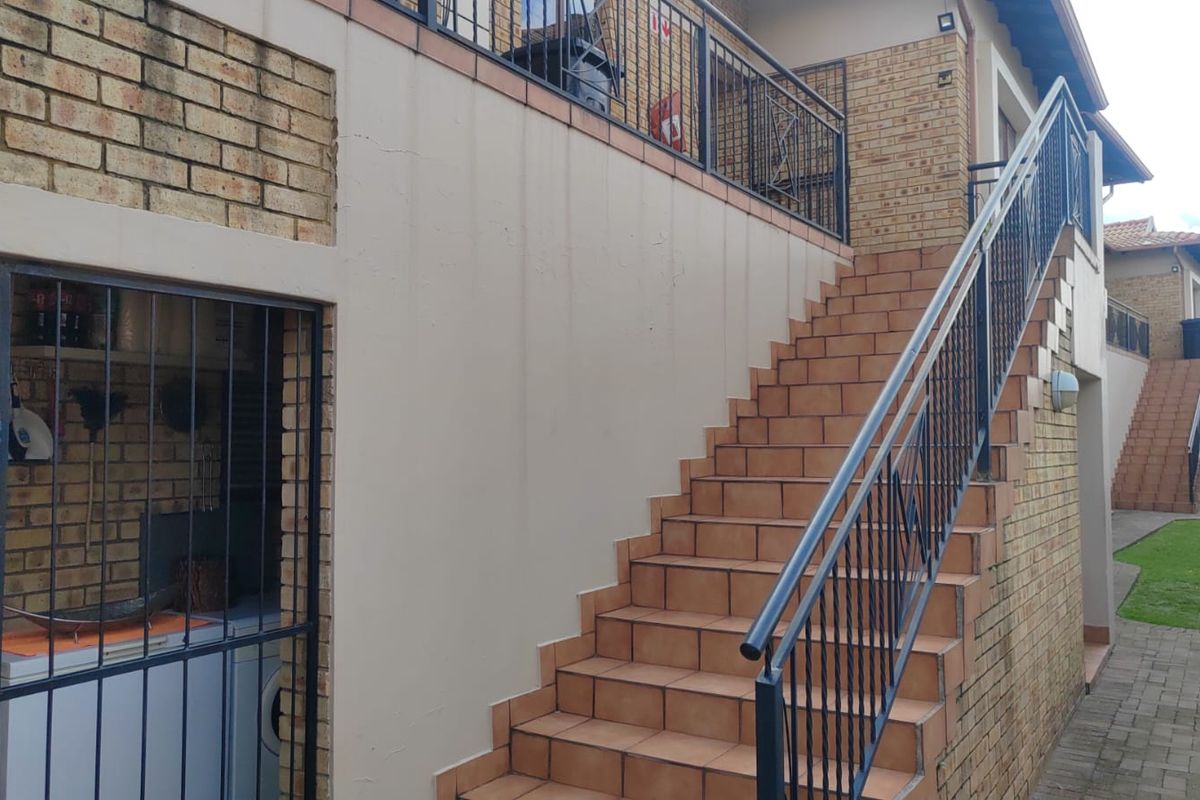 Exterior view of an apartment complex featuring a tiled staircase with metal railings leading to an upper level and a ground-level utility area.