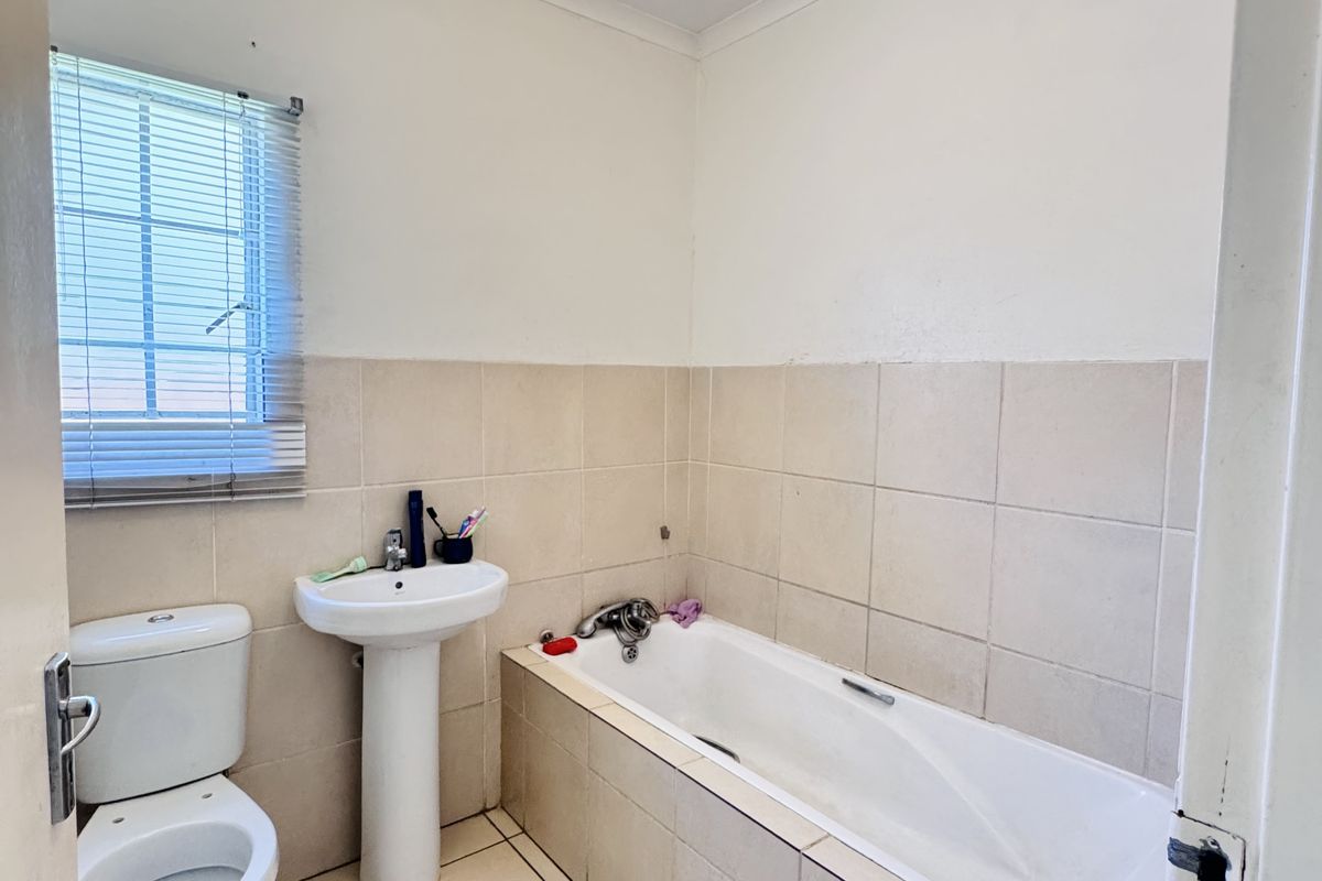 A functional bathroom featuring a standard bathtub, pedestal sink, and toilet with neutral wall and floor tiling.