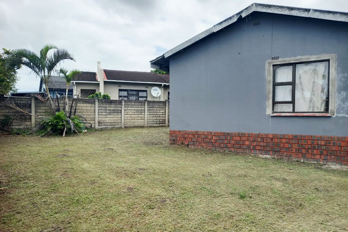 A view of the rear garden area featuring a grey painted exterior wall with a brick base and a perimeter boundary wall.