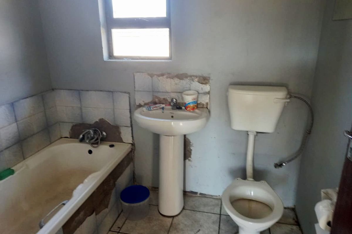 A dated bathroom featuring a pedestal basin, standard toilet, and bathtub with significant wall tile damage and visible wear on fixtures.
