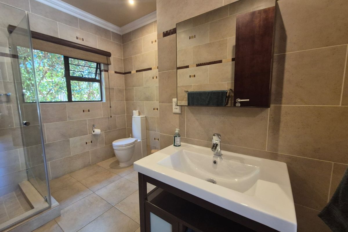 A well-maintained bathroom featuring a glass-enclosed shower, a modern vanity with a basin, a wall-mounted mirror cabinet, and neutral floor-to-ceiling tiling.