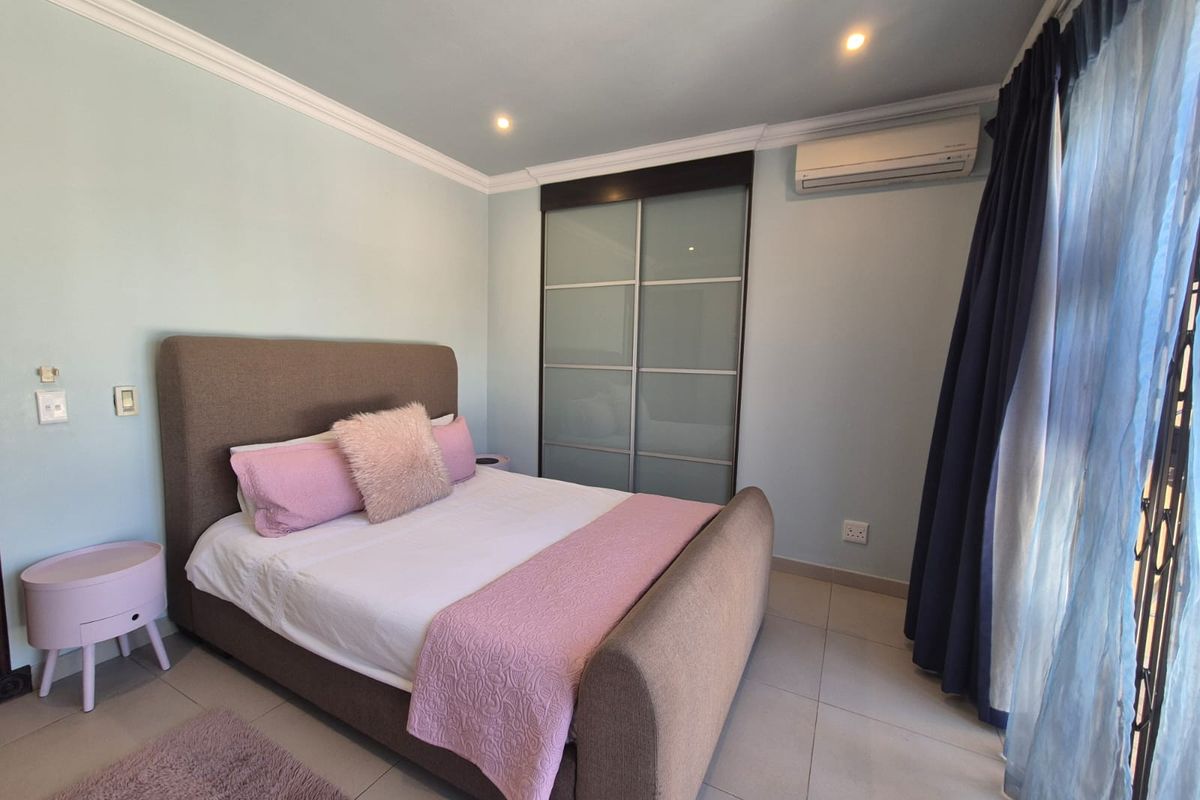 A well-maintained bedroom featuring tiled flooring, built-in sliding door cupboards, and a wall-mounted air conditioning unit.