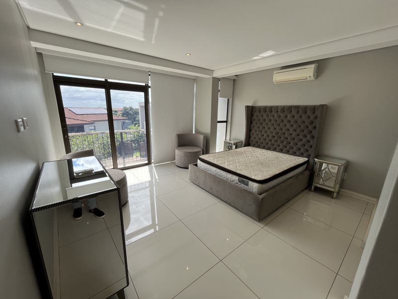 Spacious bedroom featuring large format floor tiles, recessed ceiling lighting, a wall-mounted air conditioning unit, and sliding glass doors leading to a private balcony.